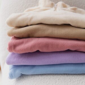 Stack of colorful fleece jackets on cozy armchair by window