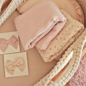 Soft pastel baby accessories including blankets and bows in a woven basket